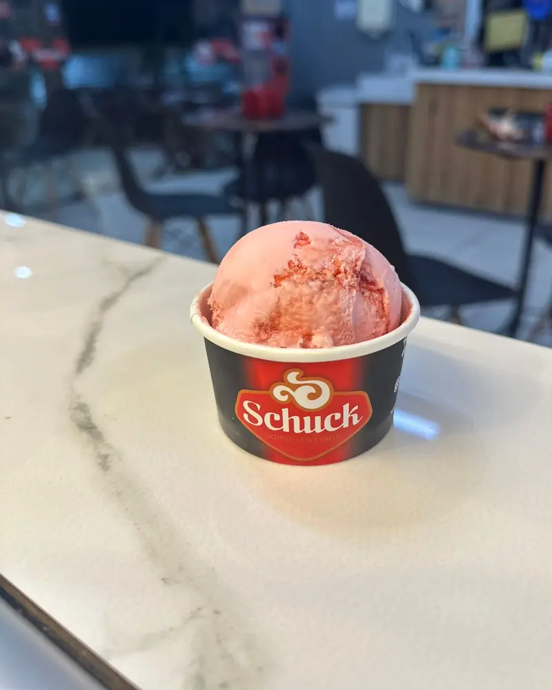 Copinho da Schuck com uma bola de sorvete rosado, em cima do balcão de mármore da loja