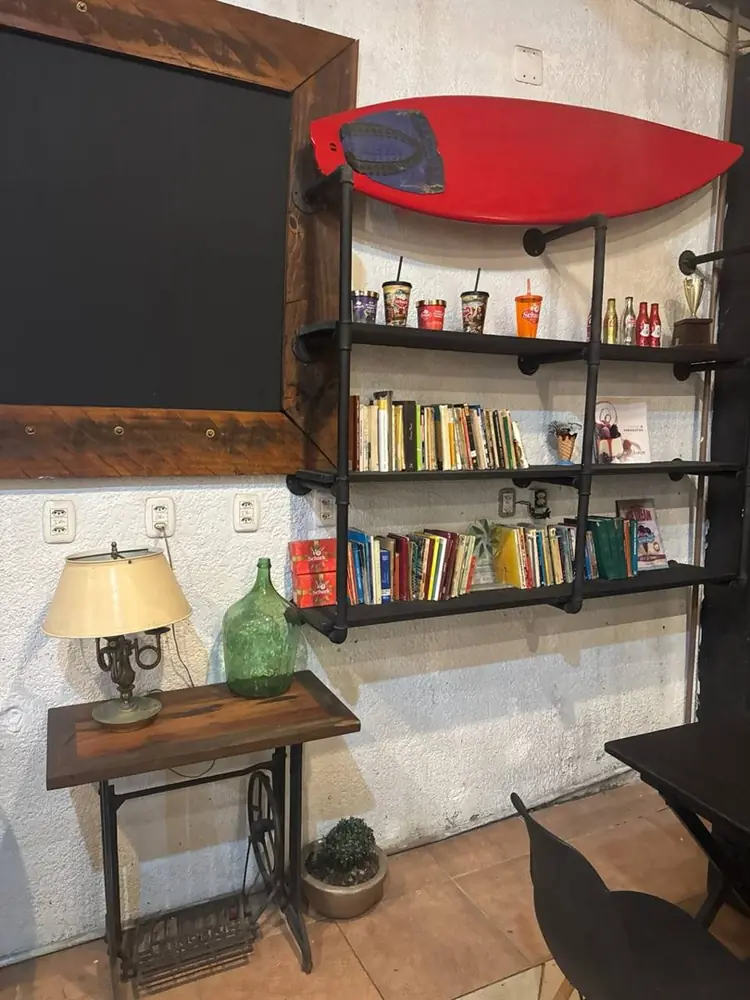 Cantinho com estante de livros, abajur e a prancha vermelha da Schuck