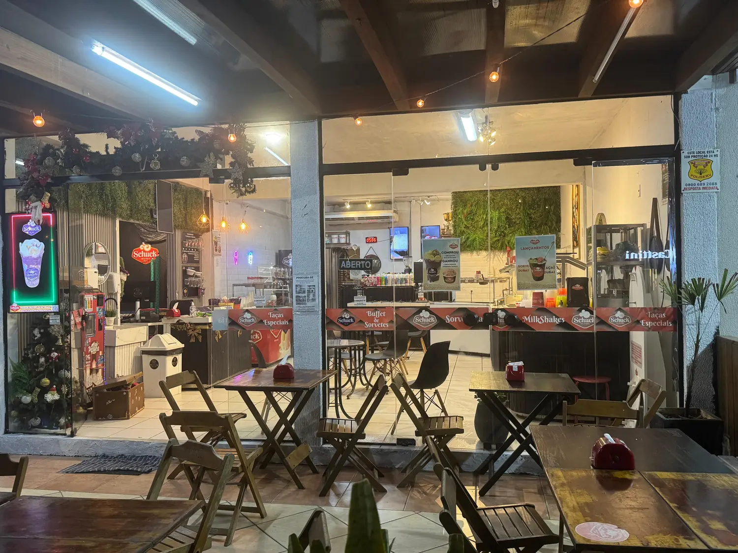 Frente envidraçada da loja à noite, com mesas e o balcão ao fundo