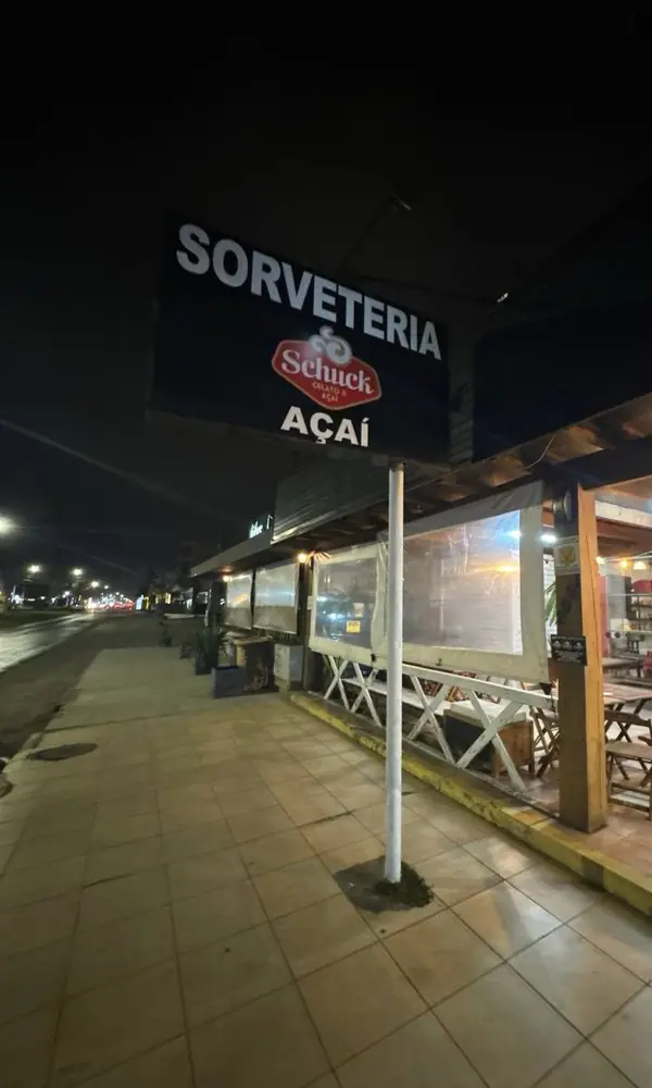 Placa Sorveteria Schuck Açaí acesa à noite, na calçada da avenida